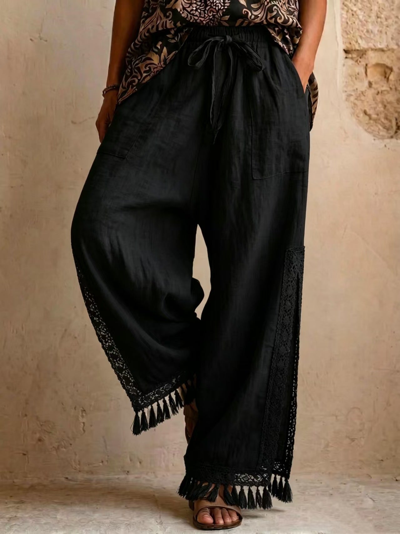 Women's bohemian lace tassel wide-leg pants in black, featuring a drawstring waist, side slit with fringe trim, and a flowing silhouette.