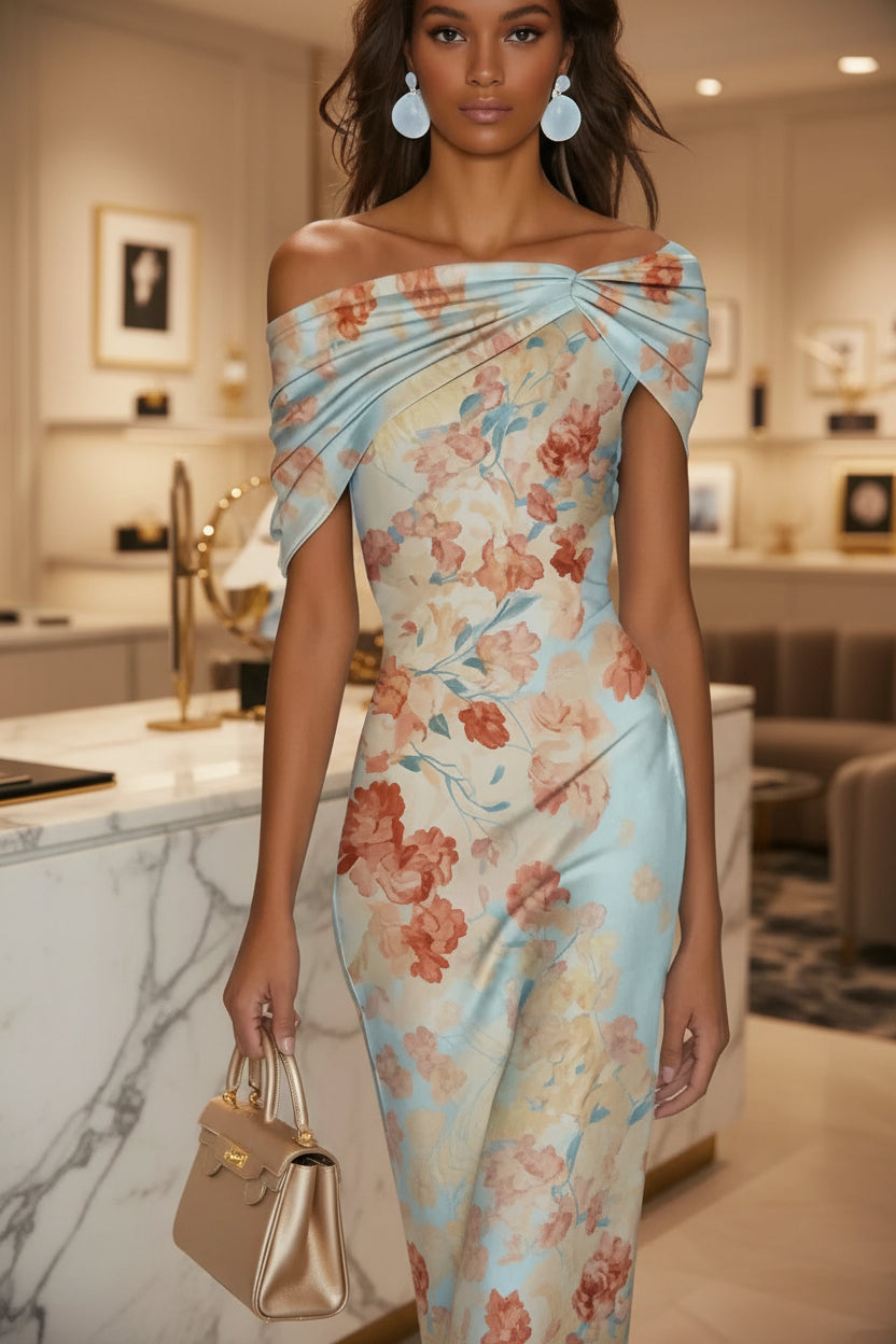 Woman wearing a light blue floral draped off-the-shoulder dress with a structured bodice, styled with drop earrings and a metallic gold handbag.