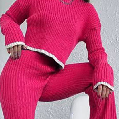 Woman wearing a vibrant pink ribbed knit two-piece set featuring a long-sleeve crop top and matching pants with white trim detail, posing indoors.