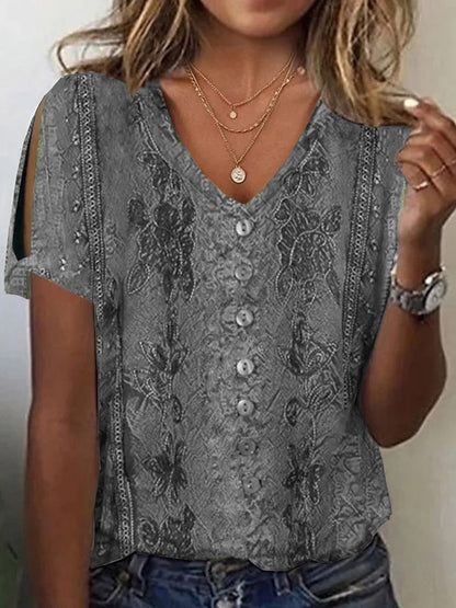 Woman wearing a gray short-sleeve V-neck top with button accents, cold-shoulder cutouts, subtle printed patterns, and layered necklaces.
