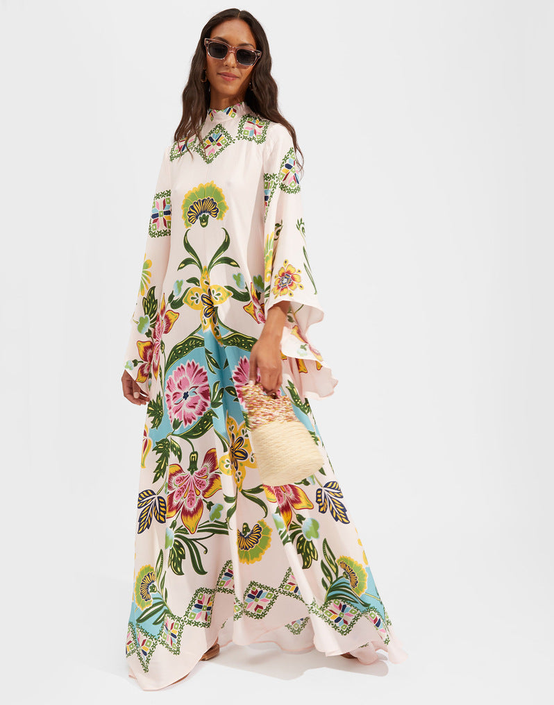 Women's floor-length A-line maxi dress in soft pink/off-white featuring a high mock stand collar, wide 3/4 flared sleeves, and a colorful botanical floral print with vibrant pink, yellow, and teal accents.
