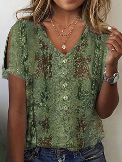 Woman wearing an olive green short-sleeve V-neck top featuring cold-shoulder cutouts, button accents, and intricate printed floral patterns, layered with delicate necklaces.