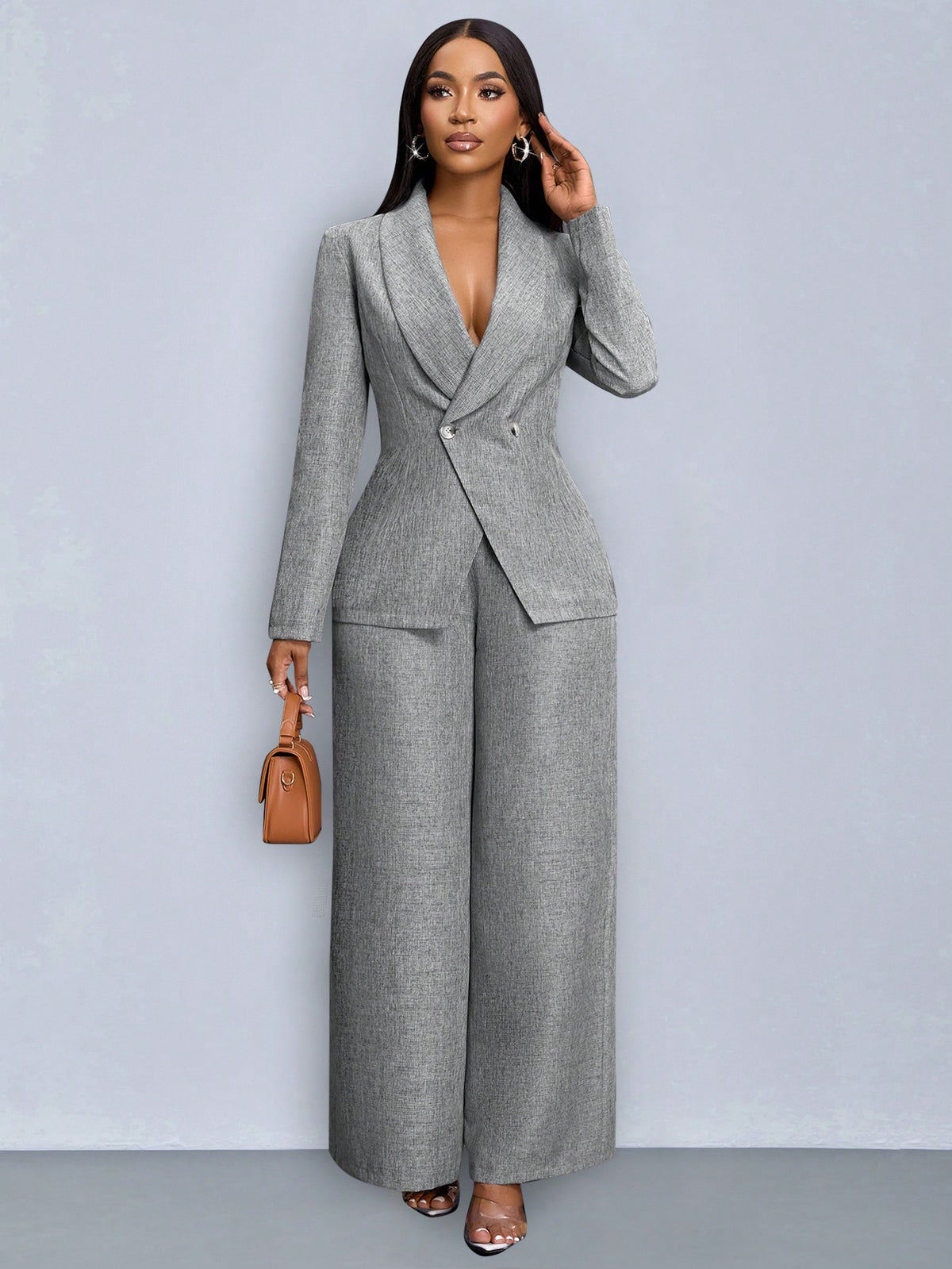 Front view of a woman posing in a grey double-breasted suit jacket with high-waisted wide-leg trousers, carrying a tan handbag.