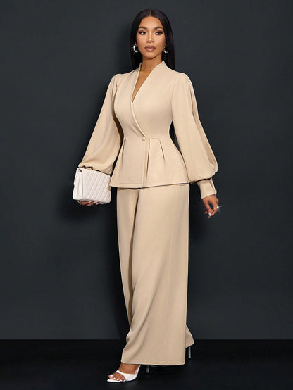 Front three-quarter view of a woman posing in an apricot beige suit set featuring a V-neck peplum blazer with pinched pleat details and long bishop slit sleeves, styled with matching wide-leg trousers and a white clutch bag.