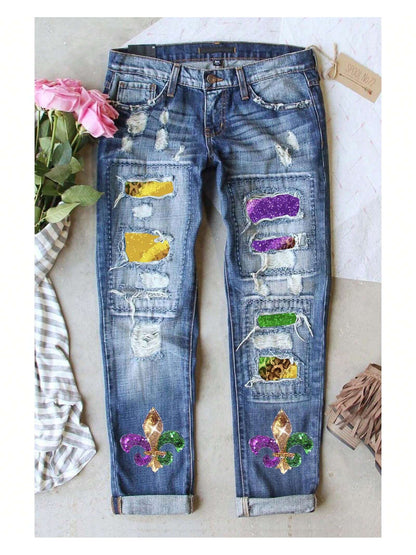 Azura Exchange sky blue distressed denim jeans laid flat, featuring shiny sequined animal-print patches, colorful fleur-de-lis details, and pink roses alongside the waistband.