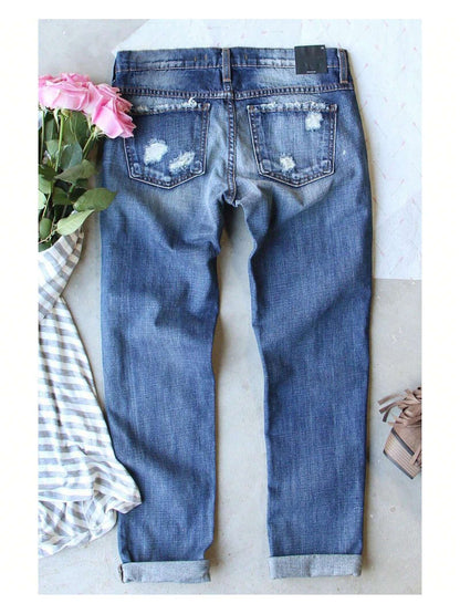 Rear view of Azura Exchange sky blue distressed denim jeans laid flat, showing back pockets, frayed distressing, and cuffed hems next to pink roses