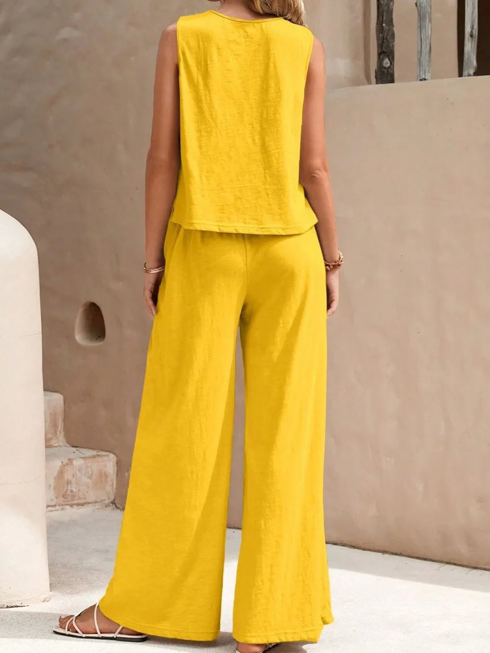 Back view of model wearing a gold yellow sleeveless round neck top and high-waisted wide leg pants set with sandals