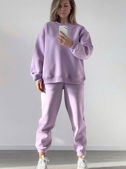 Woman wearing a purple loose-fit crewneck sweatshirt and matching jogger pants two-piece set, taking a mirror selfie with a smartphone