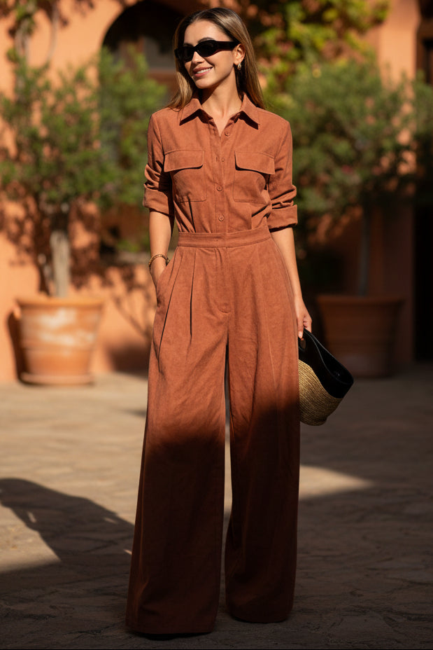Full-length model shot of a woman wearing a loose-fit, collared long-sleeve jumpsuit in dark brown with chest utility pockets and wide-leg trousers.