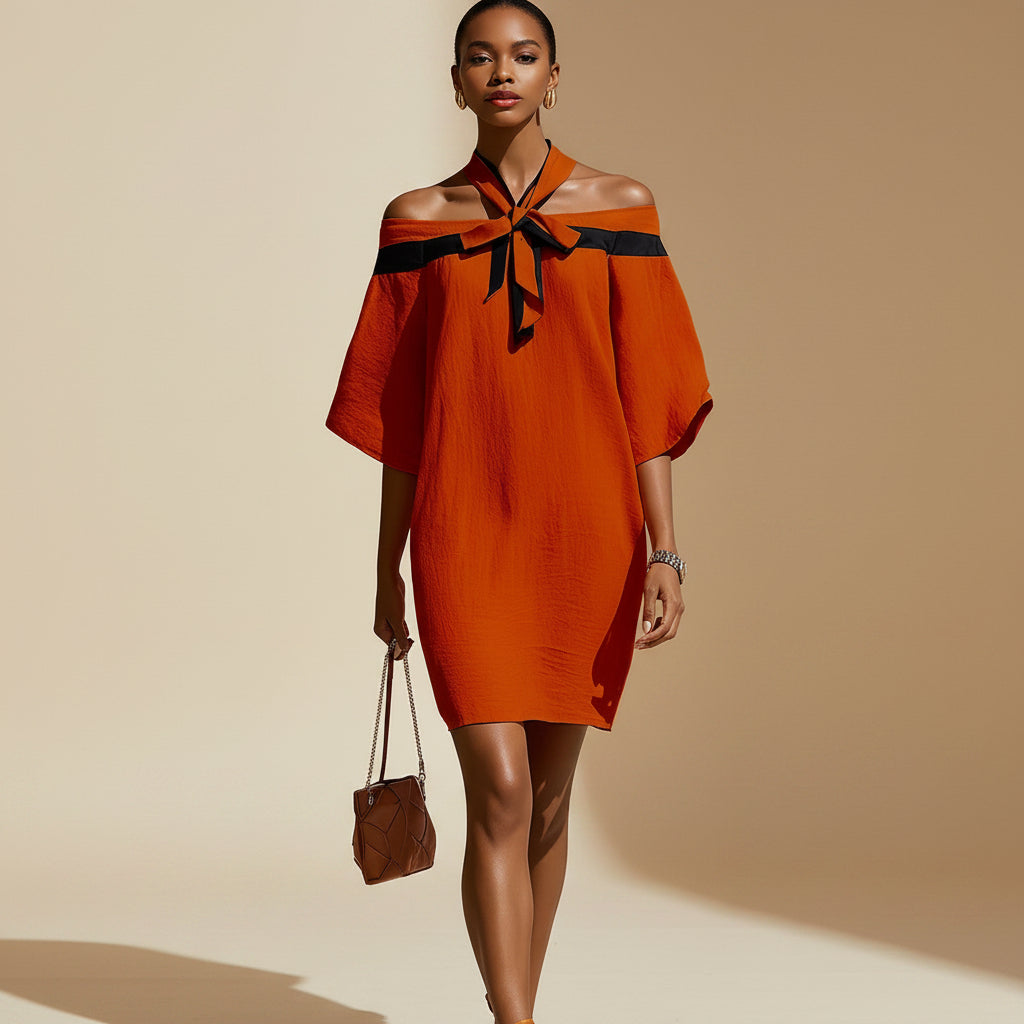 Woman wearing an orange-red off-the-shoulder A-line mini dress with a contrasting black bow collar, 3/4 sleeves, and holding a handbag.