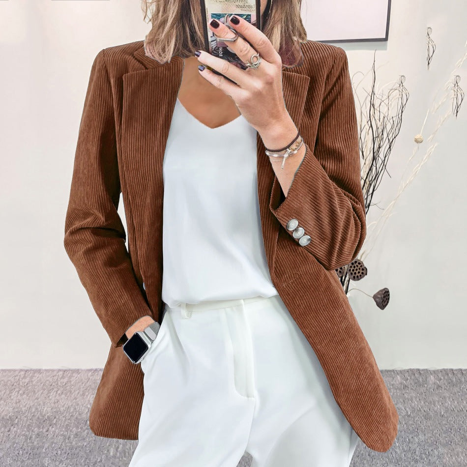 A woman wearing a caramel slim-fit corduroy blazer over a white top and white trousers, taking a mirror selfie indoors.