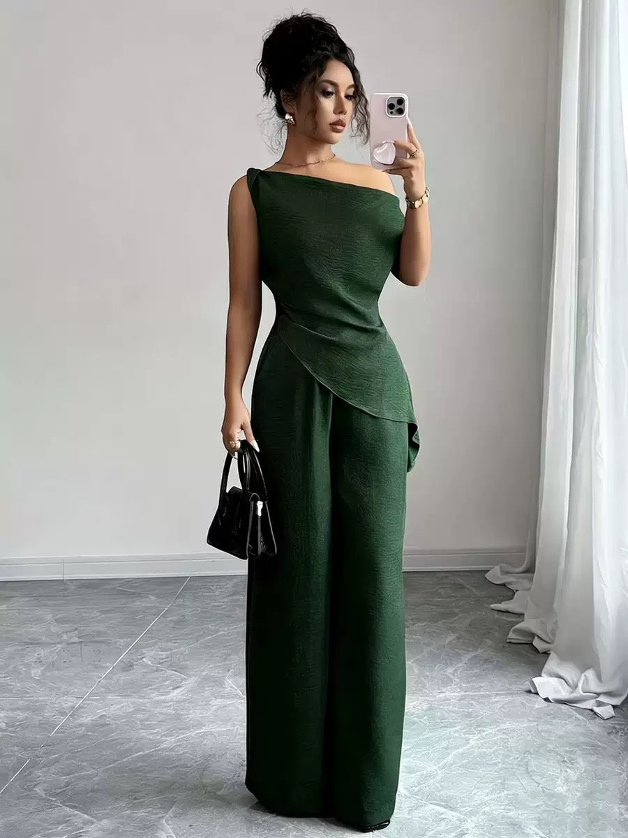 Woman taking a mirror selfie wearing a dark green casual two-piece set featuring a draped off-the-shoulder top with a diagonal front fold and matching high-waisted wide-leg pants, holding a black handbag and smartphone.