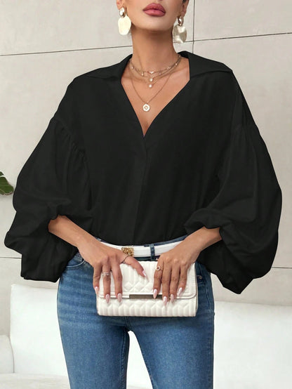 Woman wearing a navy blue polka dot V-neck top with long bubble sleeves and blue jeans.
