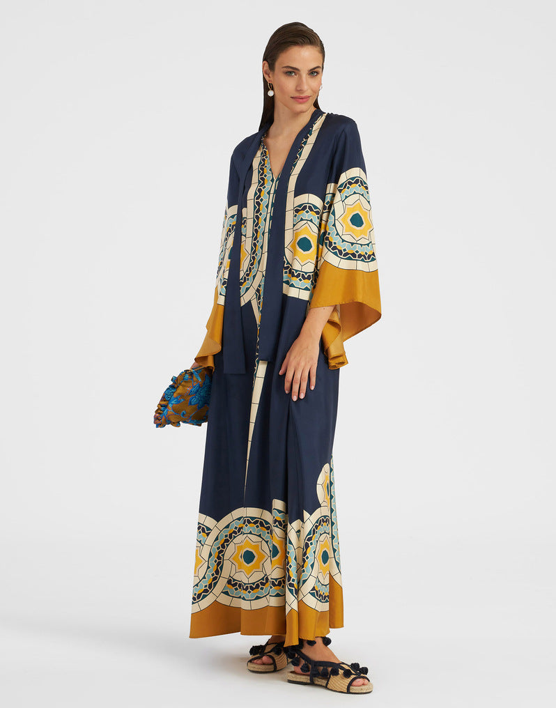 Women's floor-length A-line maxi dress in dark navy blue featuring a vibrant yellow and white circular tile and botanical print, split V-neckline, wide mustard-yellow sleeve cuffs, and decorative vertical border trim.