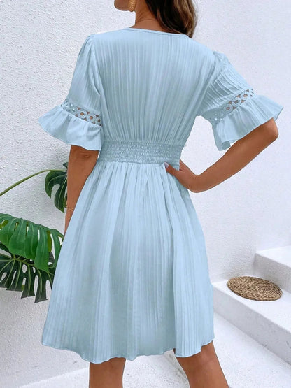 Back view of a woman wearing a light blue V-neck mini dress featuring short flounce sleeves with crochet lace trim, textured vertical striping, and a cinched lace waistband