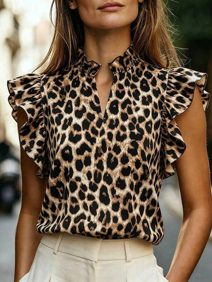 Woman wearing a leopard print sleeveless top with a high ruffle-trim mock neck and lotus-leaf ruffle sleeves, styled with cream high-waist pants.
