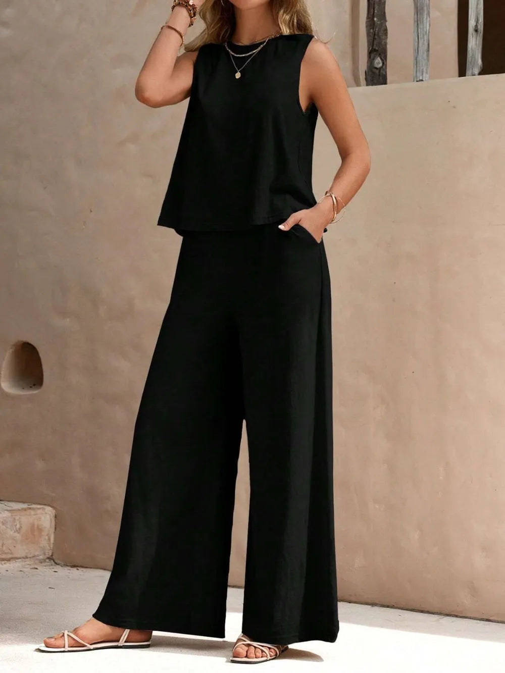 Front view of model wearing a black sleeveless round neck top and high-waisted wide leg pants set with sandals