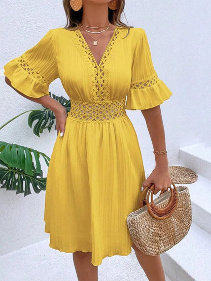 Woman wearing a bright yellow V-neck mini dress with textured vertical striping, featuring crochet lace trim along the V-neckline, waist cutouts, and flounce sleeves, accessorized with layered gold pendant necklaces and holding a woven straw handbag.