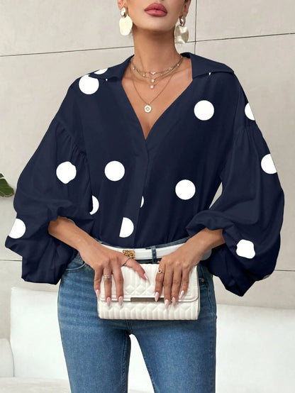 Woman wearing a navy blue polka dot V-neck long-sleeve top with bubble sleeves and blue jeans.