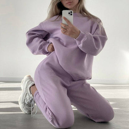 Woman wearing a purple loose-fit crewneck sweatshirt and matching jogger pants two-piece set, styled with white sneakers.