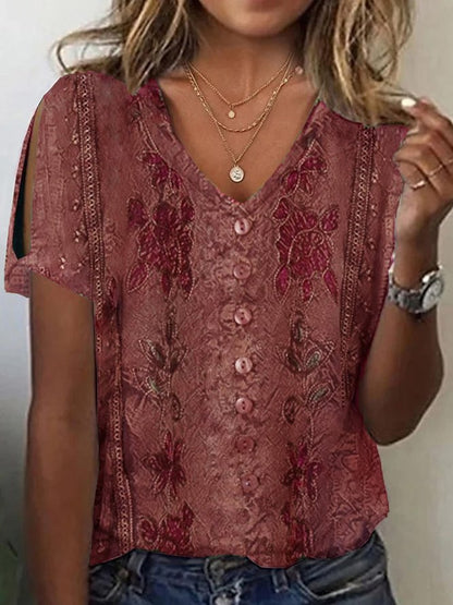 Woman wearing a burgundy short-sleeve V-neck top with button accents, cold-shoulder cutouts, subtle printed patterns, and layered necklaces.