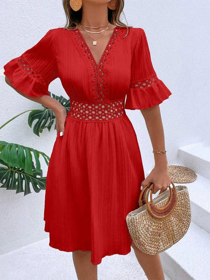 Woman wearing a vibrant red V-neck mini dress with textured vertical striping, featuring crochet lace trim along the neckline, waist cutouts, and flounce sleeve cuffs, accessorized with layered gold necklaces and holding a woven straw handbag.