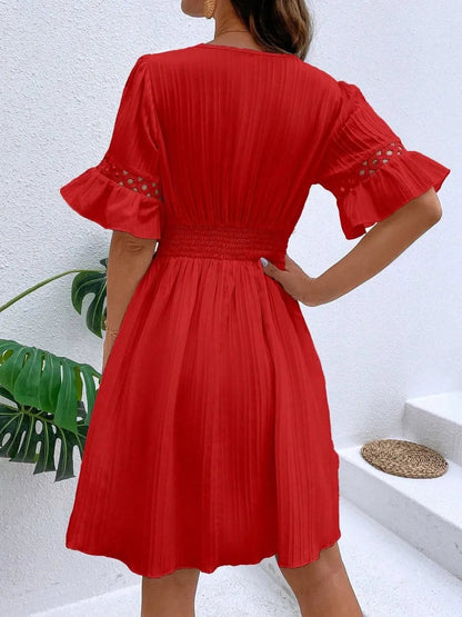 Back view of a woman wearing a vibrant red V-neck mini dress featuring short flounce sleeves with crochet lace trim, textured vertical striping, and a cinched lace waistband.
