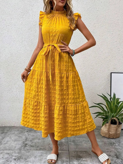 Front view of model wearing a gold yellow ruffled cap sleeve midi dress with a tied waist and white slide sandals