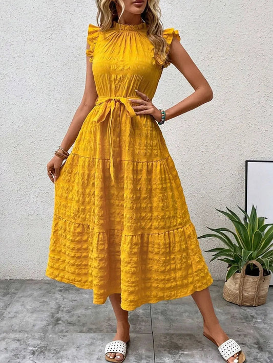 Front view of model wearing a gold yellow ruffled cap sleeve midi dress with a tied waist and white slide sandals