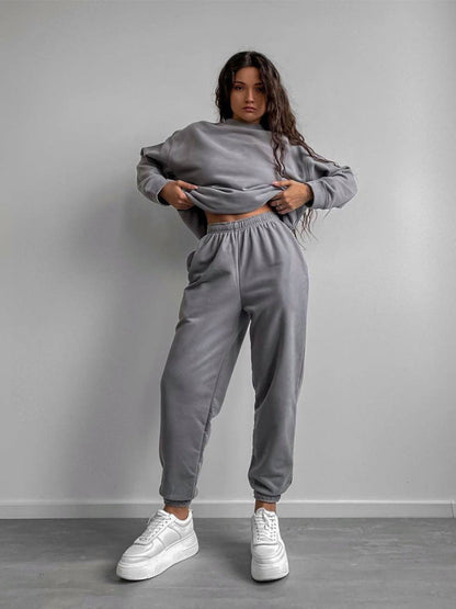 Woman wearing a gray loose-fit crewneck sweatshirt and matching jogger pants two-piece set, styled with white sneakers.
