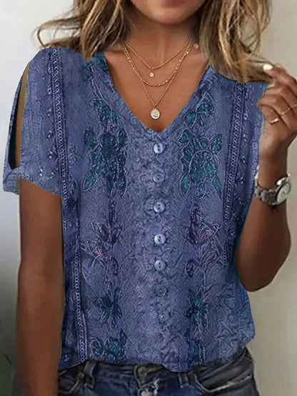Woman wearing a blue short-sleeve V-neck top with button accents, cold-shoulder cutouts, and subtle printed patterns, layered with delicate necklaces.