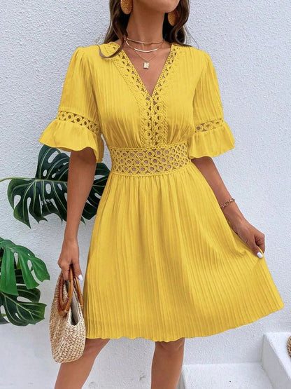 Woman wearing a bright yellow V-neck mini dress with textured vertical striping, featuring crochet lace trim along the V-neckline, waist cutouts, and flounce sleeves, styled with layered gold necklaces and holding a woven straw handbag.