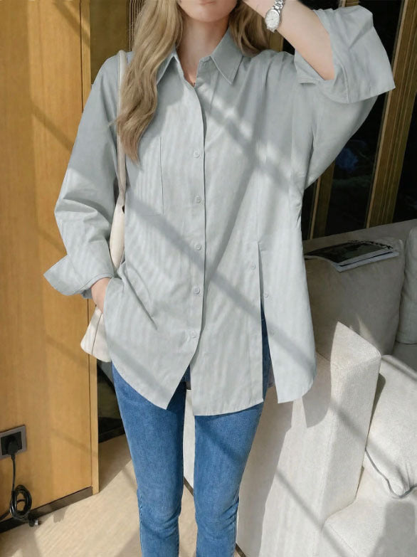 Woman wearing a sage green oversized long sleeve button-up shirt with high side slits, paired with light wash blue jeans.