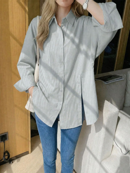 Woman wearing a sage green oversized long sleeve button-up shirt with high side slits, paired with light wash blue jeans.