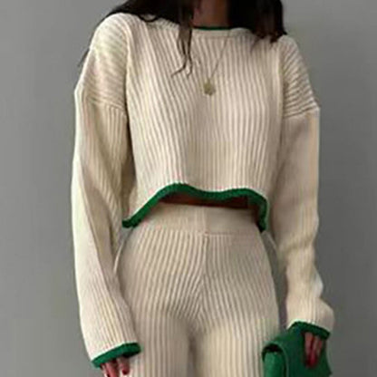 Woman wearing a white ribbed knit two-piece set featuring a long-sleeve crop top and matching pants, accented with green trim, standing indoors.