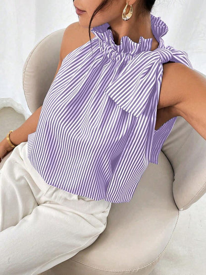Side-profile view of a model sitting down wearing a purple and white striped sleeveless top with a ruffled high neck and shoulder bow detail.