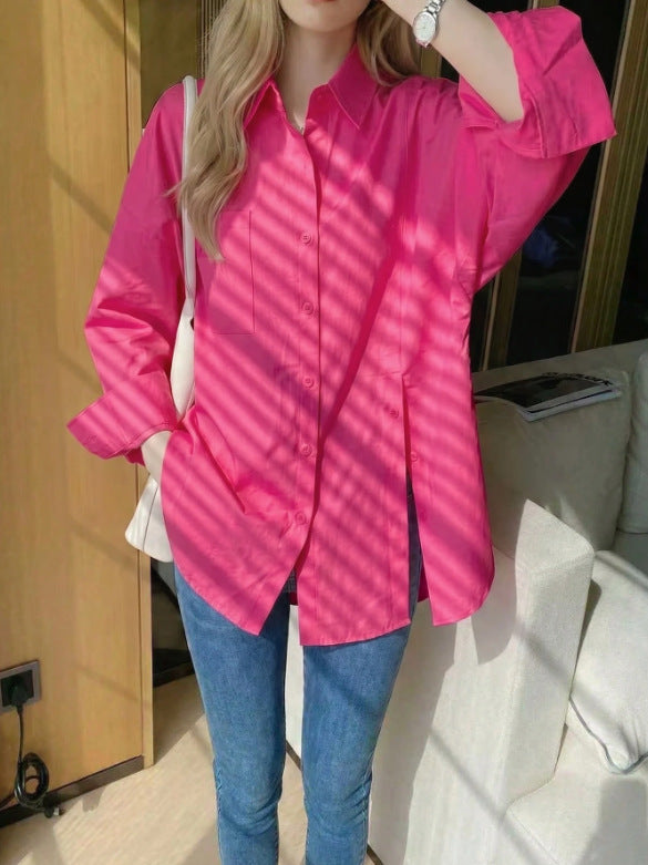 Woman wearing a bright rose red oversized long sleeve button-down shirt styled with blue jeans and a white shoulder bag.