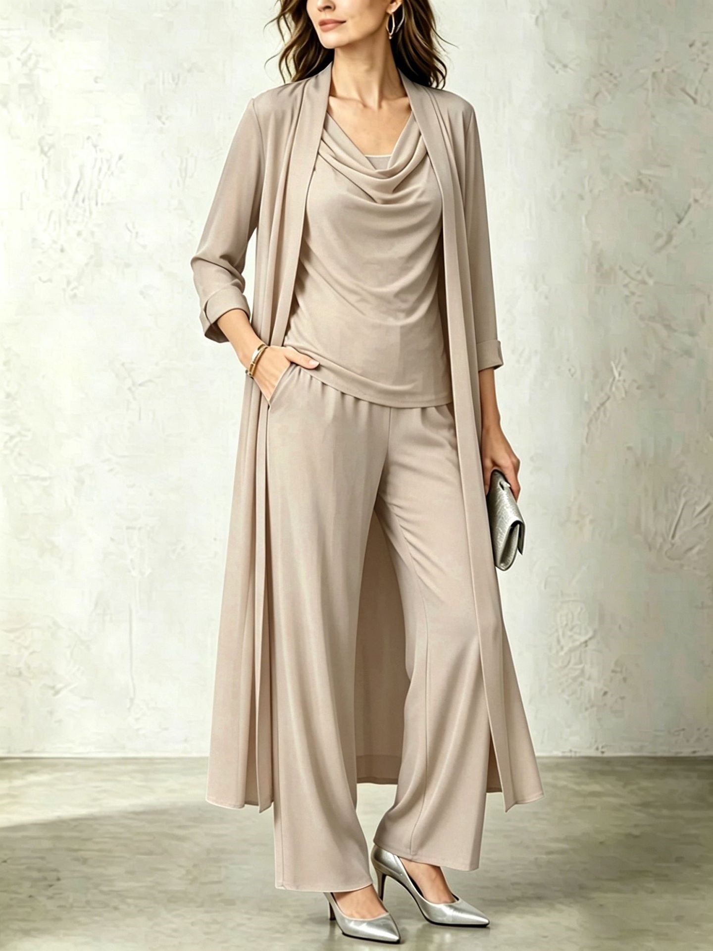Beige three-piece women's outfit featuring a long open duster cardigan, cowl neck top, and fluid wide-leg pants.