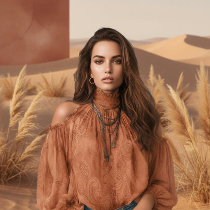 Front view of a woman standing outdoors in a desert landscape with dried grass, wearing a caramel brown retro cashew print off-shoulder blouse with lantern sleeves and layered necklaces.