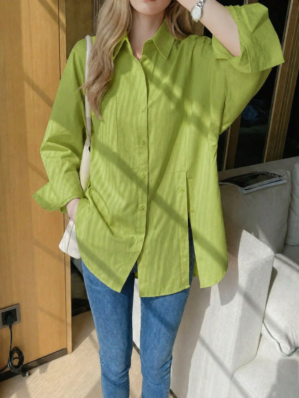 Woman wearing a light yellow oversized long sleeve button-up shirt with high side slits, paired with blue jeans in warm, sunny light.