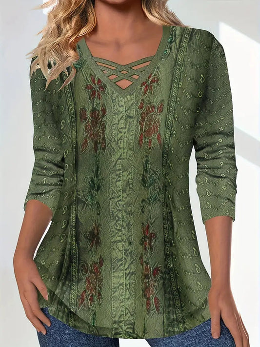 Woman wearing an olive green long-sleeve tunic top featuring a crisscross V-neckline and intricate printed floral patterns.