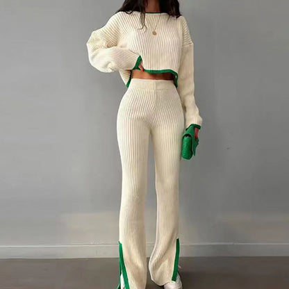 Woman wearing a white knit two-piece set with green color-block trim, featuring a long-sleeve crop top and matching slim slit pants, holding a green clutch.