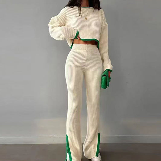 Woman wearing a white knit two-piece set with green color-block trim, featuring a long-sleeve crop top and matching slim slit pants, holding a green clutch.