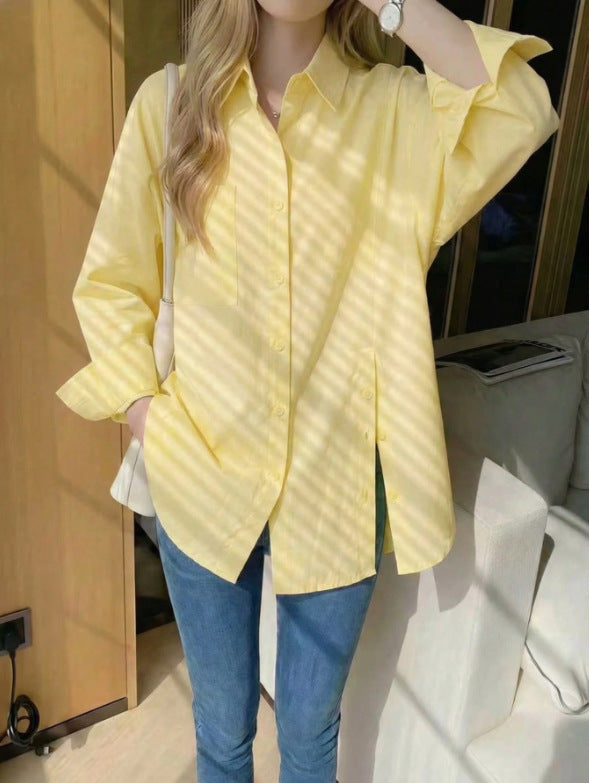 Woman wearing a light yellow oversized long sleeve button-up shirt with high side slits, paired with blue jeans in warm, sunny light.