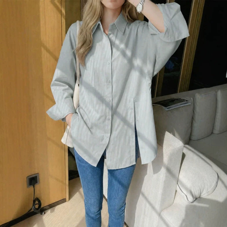 Woman wearing a light gray oversized long sleeve button-up shirt with side slits and drop shoulders, paired with blue jeans.