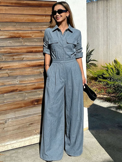 Woman in a blue-gray collared long-sleeve jumpsuit with chest flap pockets, sunglasses, and wide-leg trousers.