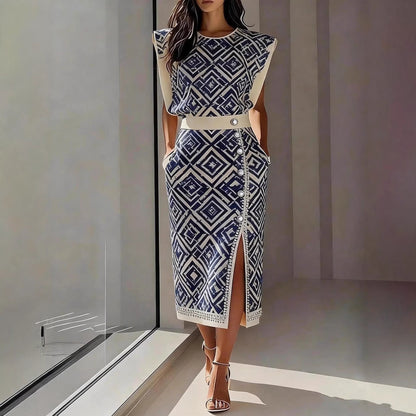 Model standing in a modern interior wearing a blue and white geometric printed sleeveless top and matching high-slit maxi skirt set.