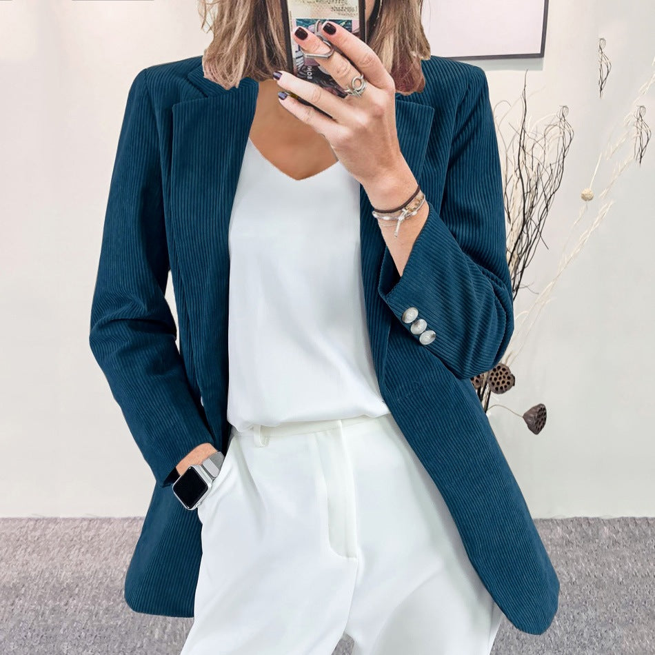 Woman wearing a dark green slim-fit corduroy blazer over a white top and white trousers, taking a mirror selfie indoors.