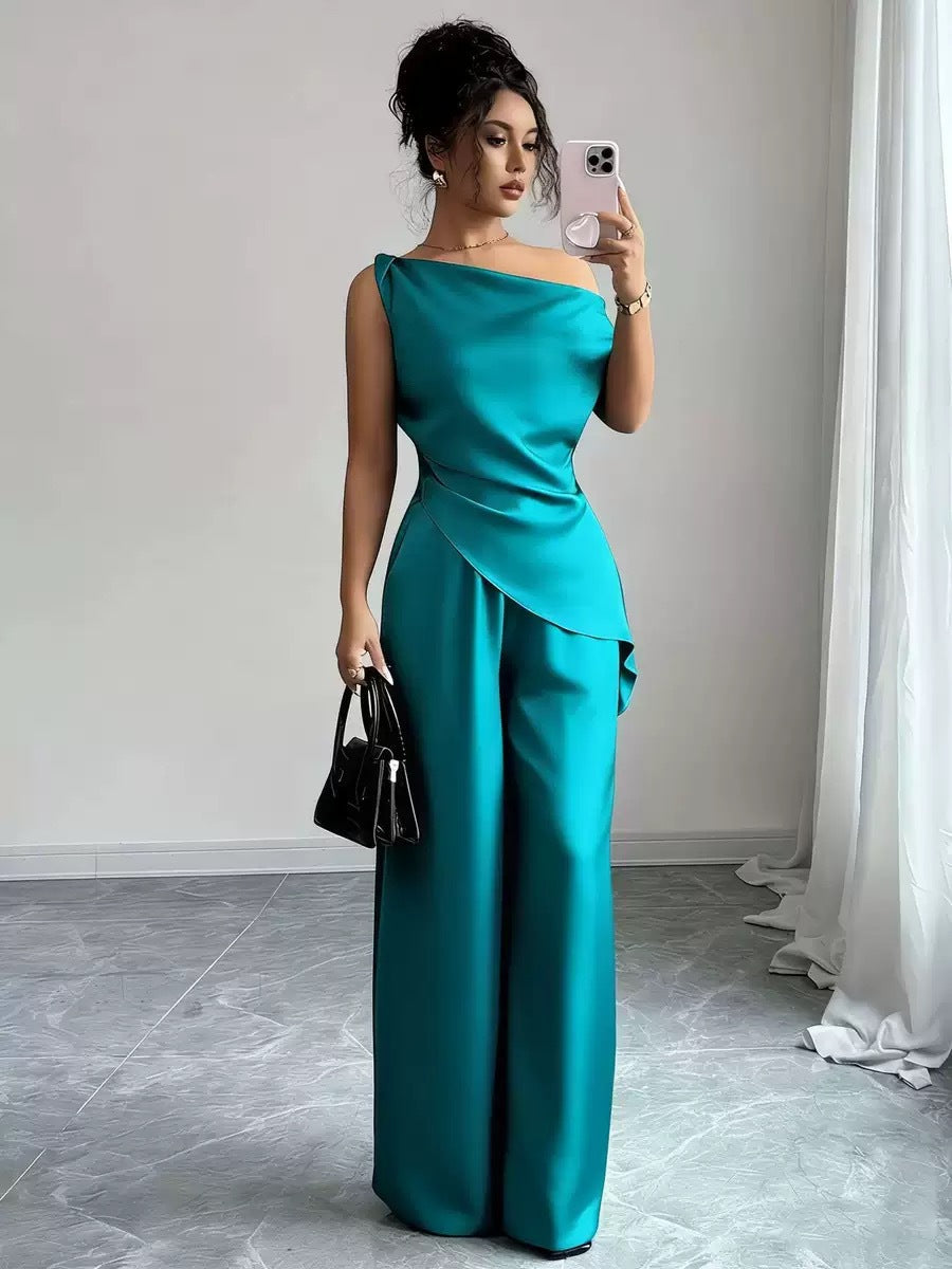 Woman taking a mirror selfie wearing a dark green casual two-piece set featuring a draped off-the-shoulder top with a diagonal front fold and matching high-waisted wide-leg pants, holding a black handbag and smartphone.