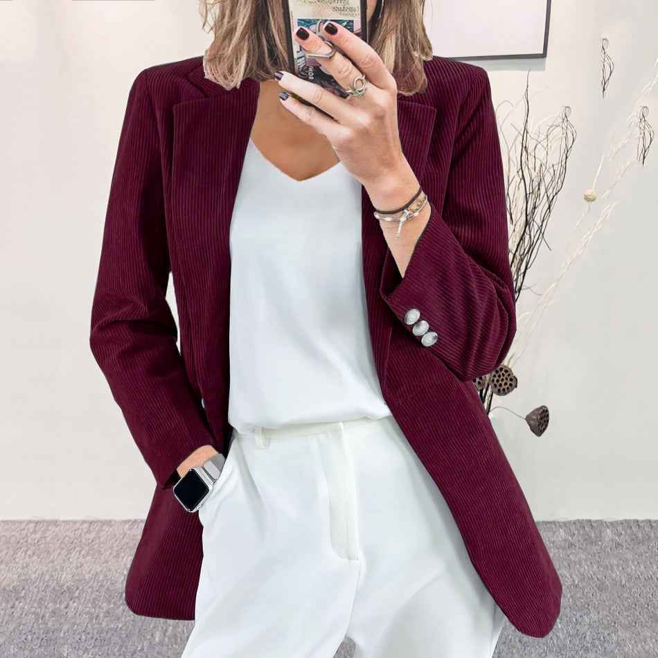 Woman wearing a dark green slim-fit corduroy blazer over a white top and white trousers, taking a mirror selfie indoors.